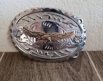 May include: Silver belt buckle with an ornate design and a gold eagle in the center.