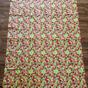 May include: A rectangular fabric with a repeating pattern of red chili peppers on a yellow background with green leaf accents. The fabric is folded and laid out on a wooden surface.