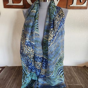 May include: A patterned scarf in shades of blue and green, draped over a mannequin. The scarf displays a mix of animal prints, including leopard and zebra stripes. The word "LOVE" is visible in the background, mounted on a wooden surface.