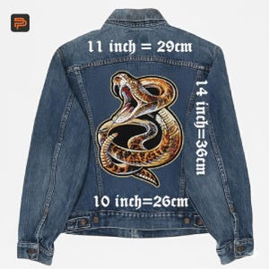May include: Denim jacket in blue with a snake patch on the back. The snake design features brown, tan, and red colours. The patch measures 29cm by 36cm. The jacket is a classic style.