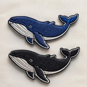 以下が含まれることがあります： 濃い青と黒の2種類のクジラの刺繍ワッペン。どちらも白い腹部のディテール、はっきりとした目、湾曲した尾びれが特徴で、布製品に簡単に取り付けられるよう白いステッチの縁取りが施されています。