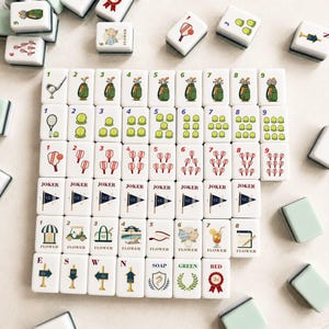 May include: A set of white Mahjong tiles with various illustrations, including golf clubs, tennis rackets, and floral designs. The tiles feature numbers, Jokers, and directional markers. Some tiles have the word "FLOWER".