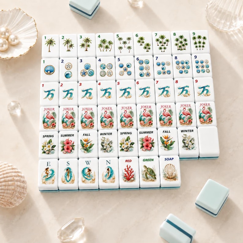 May include: A set of white Mahjong tiles with various illustrations, including palm trees, seashells, and flamingos. The tiles are arranged on a light surface, with small blue boxes and seashells nearby. The tiles feature numbers, suits, and seasonal themes.