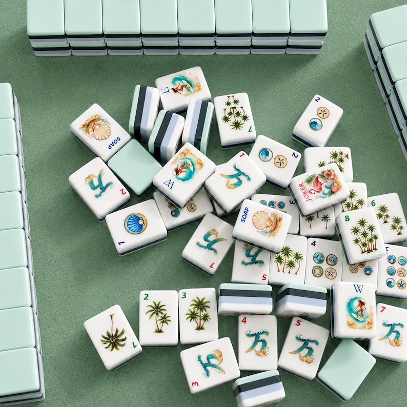 May include: A collection of white Mahjong tiles with various illustrations, including palm trees, shells, and figures. The tiles are arranged on a green surface, with some tiles stacked and others scattered. The set includes tiles with the word "SOAP" and numbers.
