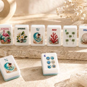 May include: A collection of white Mahjong tiles with colorful illustrations. The tiles feature images of a flamingo, flowers, a surfer, coral, palm trees, and a seashell. Some tiles have text such as "JOKER", "SPRING", "RED", "SOAP", and numbers.