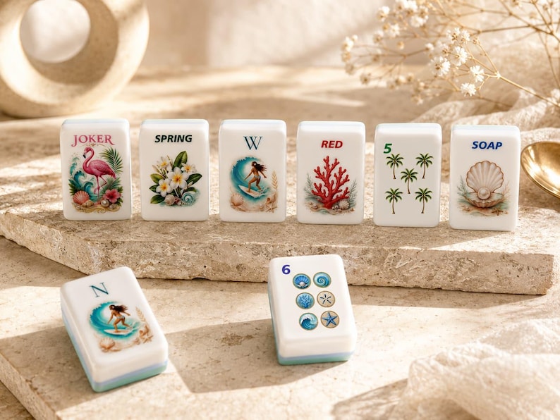 May include: A collection of white Mahjong tiles with colorful illustrations. The tiles feature images of a flamingo, flowers, a surfer, coral, palm trees, and a seashell. Some tiles have text such as "JOKER", "SPRING", "RED", "SOAP", and numbers.