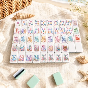 Op de afbeelding: Een complete set witte Mahjong-tegels met kleurrijke illustraties met zeethema. De tegels tonen afbeeldingen van zeepaardjes, koraal, schelpen en ander zeeleven. Inclusief groene en witte schoonmaakaccessoires.