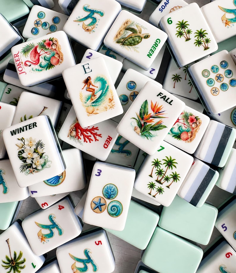 May include: A collection of white Mahjong tiles with colorful illustrations. Some tiles feature tropical scenes, a flamingo, a surfer, and floral designs. Other tiles have numbers and words like "Joker", "Winter", and "Fall".