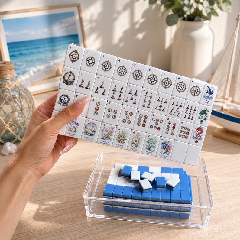 May include: A set of white mahjong tiles featuring nautical and ocean-themed illustrations, including lighthouses, anchors, and sea life. The tiles are arranged in a grid, with additional blue-backed tiles stored in a clear acrylic tray.
