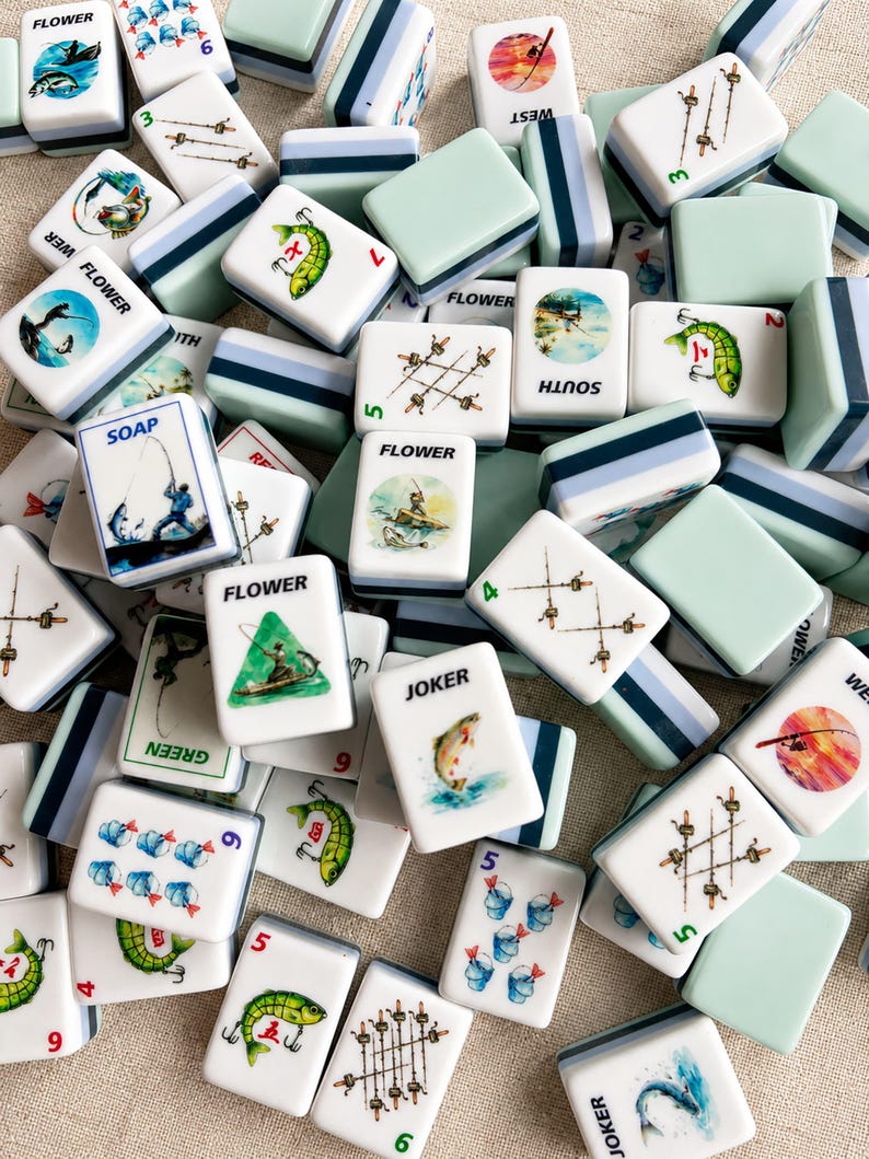 May include: A collection of white and seafoam green Mahjong tiles. The tiles feature fishing-themed illustrations, including fish, fishing rods, and boats. Some tiles have the word "FLOWER" or numbers.