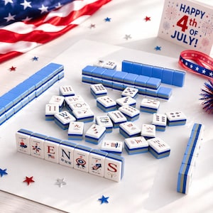 May include: A Mahjong set with blue and white tiles, arranged on a white surface with an American flag and festive decorations. The tiles feature various symbols and characters, with some spelling out "ENS". A "Happy 4th of July!" sign is also present.