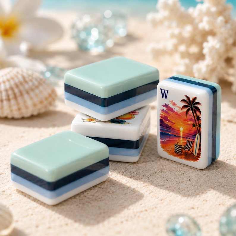 K&ouml;nnte beinhalten: Eine Sammlung farbenfroher Mahjong-Steine mit Strandmotiv. Die Steine sind auf einer sandigen Oberfl&auml;che gestapelt, wobei einige Steine eine Sonnenuntergangsszene mit Palmen, einem Surfbrett und dem Buchstaben "W" zeigen. Die Steine haben ein hellblaues, dunkelblaues und wei&szlig;es Farbschema.