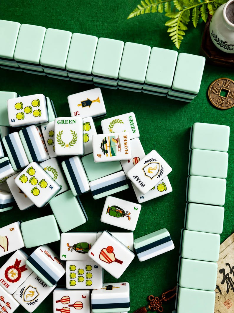 Pode incluir: Um conjunto de pe&ccedil;as retangulares de mahjong com versos em verde menta claro e faces brancas apresentando v&aacute;rias ilustra&ccedil;&otilde;es coloridas, incluindo equipamentos esportivos, coroas de flores e etiquetas de texto como GREEN, FLOWER, SOAP e RED.