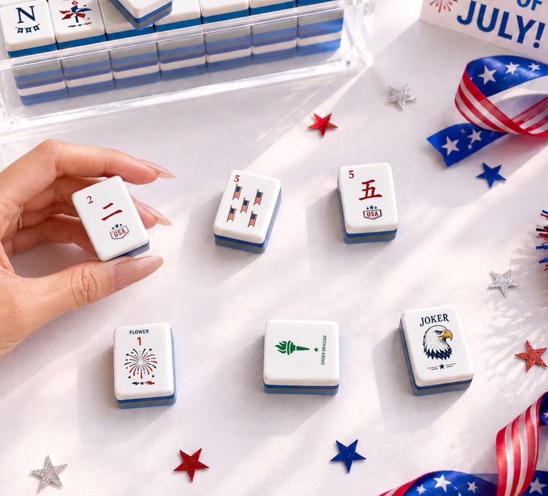May include: A collection of white and blue Mahjong tiles with various symbols and numbers, including a "Joker" tile with an eagle. The tiles are arranged with patriotic decorations like star-shaped confetti and a ribbon with stars.