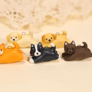 May include: A collection of small, colorful dog figurines in various poses. The dogs are in shades of yellow, orange, black, and brown, with white accents. Each figurine has a small loop for hanging.