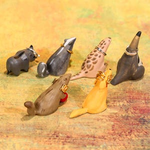 May include: A collection of six ceramic animal ring holders in various colors. The animals include a gray elephant, a badger, a spotted seal, a dark brown animal, a brown beaver with a red ball, and a yellow dog. Each animal holds a ring.