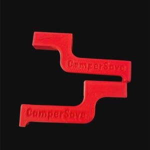 May include: Two red plastic CamperSave tools are shown against a black background. Each tool has a distinctive, curved shape with the text "CamperSave" embossed on the side. The tools appear to be designed for a specific purpose.