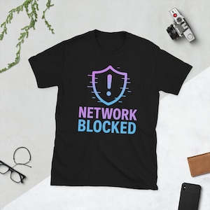 Può includere: T-shirt nera con grafica a scudo e la scritta "NETWORK BLOCKED" in blu e viola sfumato. Il design include un punto esclamativo. Il disegno è centrato sul davanti.