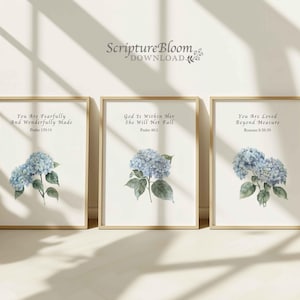 Puede incluir: Tres impresiones artísticas enmarcadas con marcos dorados. Cada impresión presenta una ilustración en acuarela de flores de hortensia azules y texto inspirador. El texto incluye versículos bíblicos: Salmo 139:14, Salmo 46:5 y Romanos 8:38-39.