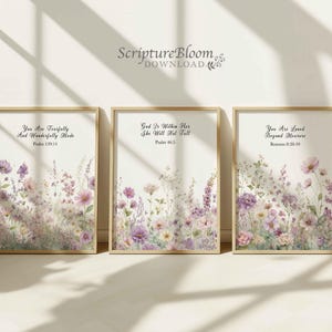 Op de afbeelding: Drie ingelijste kunstdrukken met gouden frames. Elke print heeft bloemen aquarel kunst in tinten paars, roze en wit. De prints hebben inspirerende citaten en bijbelverzen: Psalm 139:14, Psalm 46:5 en Romeinen 8:38-39. De prints worden weergegeven op een wit oppervlak.