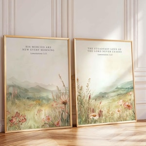 May include: Two framed art prints with gold frames. Each print features a watercolour landscape with fields of flowers and mountains in the background. The first print reads "HIS MERCIES ARE NEW EVERY MORNING" and the second reads "THE STEADFAST LOVE OF THE LORD NEVER CEASES."