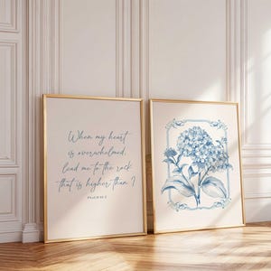 Puede incluir: Dos impresiones artísticas enmarcadas. Una presenta el texto "When my heart is overwhelmed, lead me to the rock that is higher than I. Psalm 61:2" en escritura azul. La otra impresión muestra una ilustración de hortensia azul dentro de un marco decorativo.