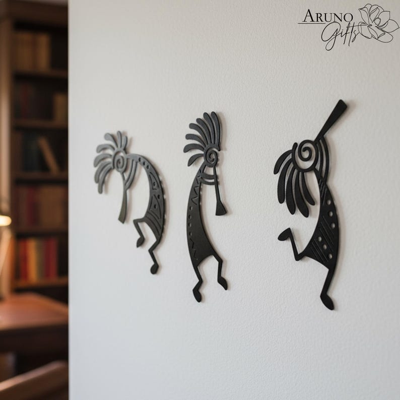 May include: Three black metal Kokopelli wall art pieces are mounted on a white wall. Each figure has a distinct design, with details like headdresses and flute-like instruments. The figures are in various poses, adding a dynamic feel to the decor.