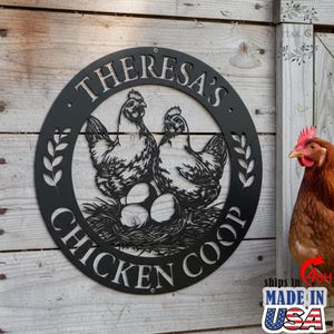 May include: Black metal sign with the text "Theresa's Chicken Coop" in a circular design. The sign features two detailed hen illustrations above a nest with eggs. The sign is mounted on a wooden background.
