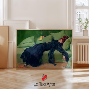 以下が含まれることがあります： 緑色のソファに横たわる黒いドレスを着た女性の絵画。彼女は黄色い本を手に持っています。絵画は木製の額縁に入っています。