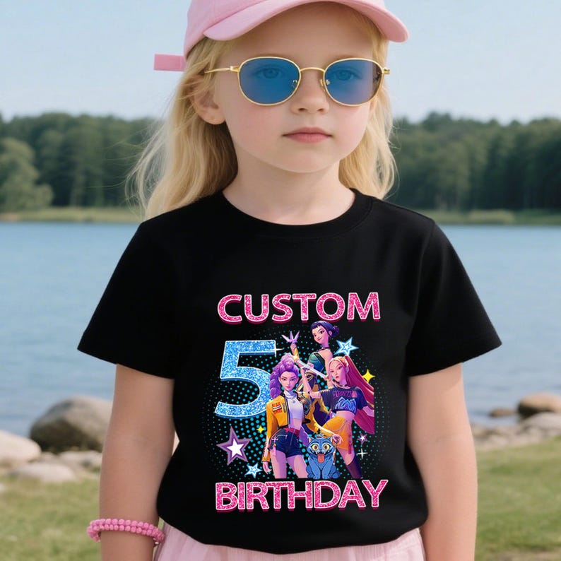 Puede incluir: Camiseta negra con un dise&ntilde;o gr&aacute;fico colorido con el texto "CUSTOM 5 BIRTHDAY". El gr&aacute;fico incluye personajes de dibujos animados y estrellas. La ni&ntilde;a de la imagen lleva una gorra rosa y gafas de sol.