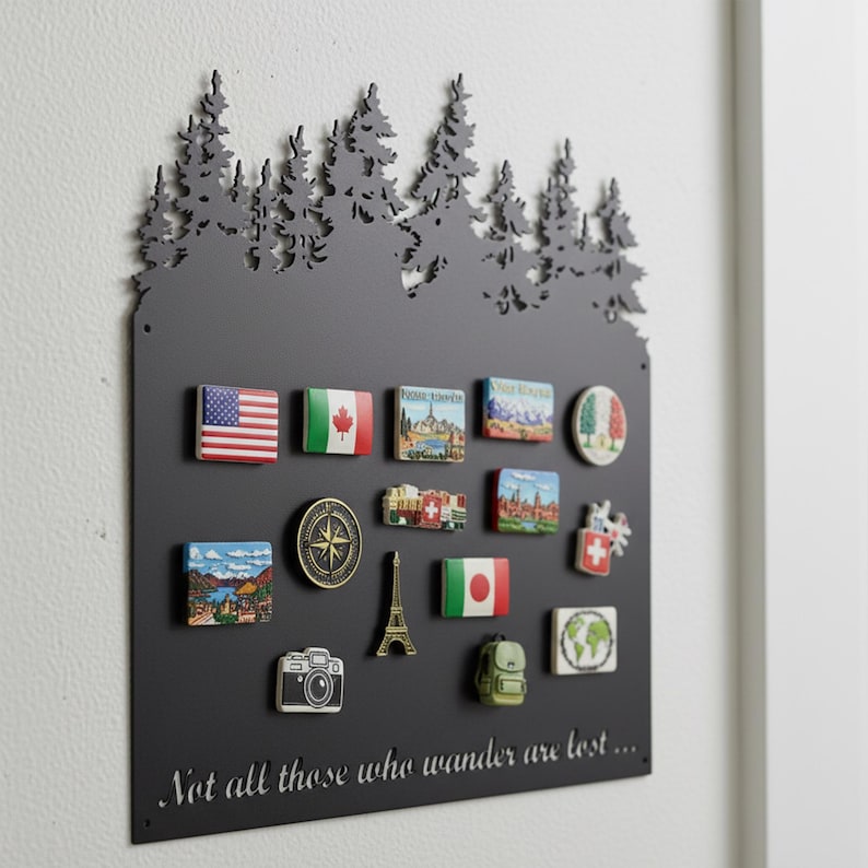 May include: A black metal magnetic board with a forest silhouette at the top, holding various travel-themed magnets. Magnets include flags, landmarks, and a compass. The text "Not all those who wander are lost..." is at the bottom.