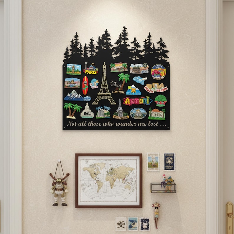 May include: A black metal travel souvenir display board with a forest silhouette at the top. The board features various travel-themed magnets, including the Eiffel Tower and the text "Not all those who wander are lost..."
