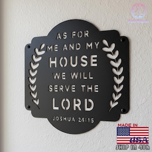 May include: Black metal wall sign with the text "AS FOR ME AND MY HOUSE WE WILL SERVE THE LORD JOSHUA 24:15". The sign has a decorative laurel wreath design and is mounted on a white wall.