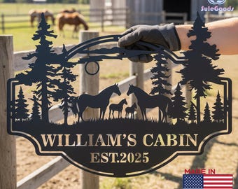 Può includere: Cartello in metallo nero con una silhouette di cavalli e alberi, con la scritta "WILLIAM'S CABIN EST.2025". Il cartello è tenuto davanti a una staccionata di legno e a un campo erboso con cavalli sullo sfondo. Fatto negli Stati Uniti.
