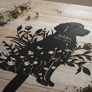 May include: Black metal dog silhouette with floral and butterfly cutouts. The dog's name, "Balchin," and the years "2015-2025" are etched on the side. The artwork is set against a light wood background, with dried flowers.