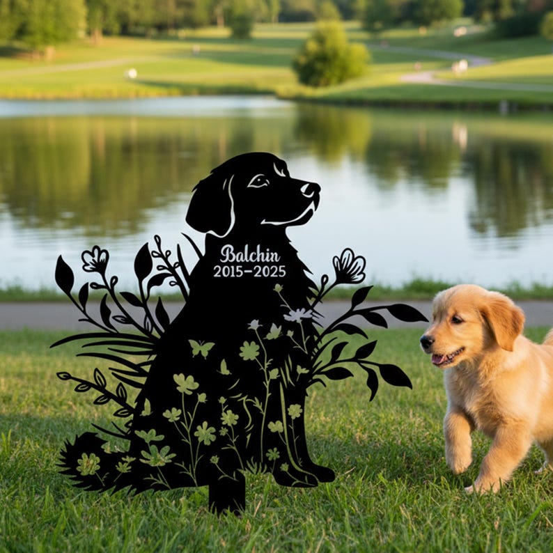 May include: Black metal dog silhouette with floral detailing, the name "Balchin" and dates "2015-2025". A golden retriever puppy is in the background on grass near a lake. The silhouette is a memorial.