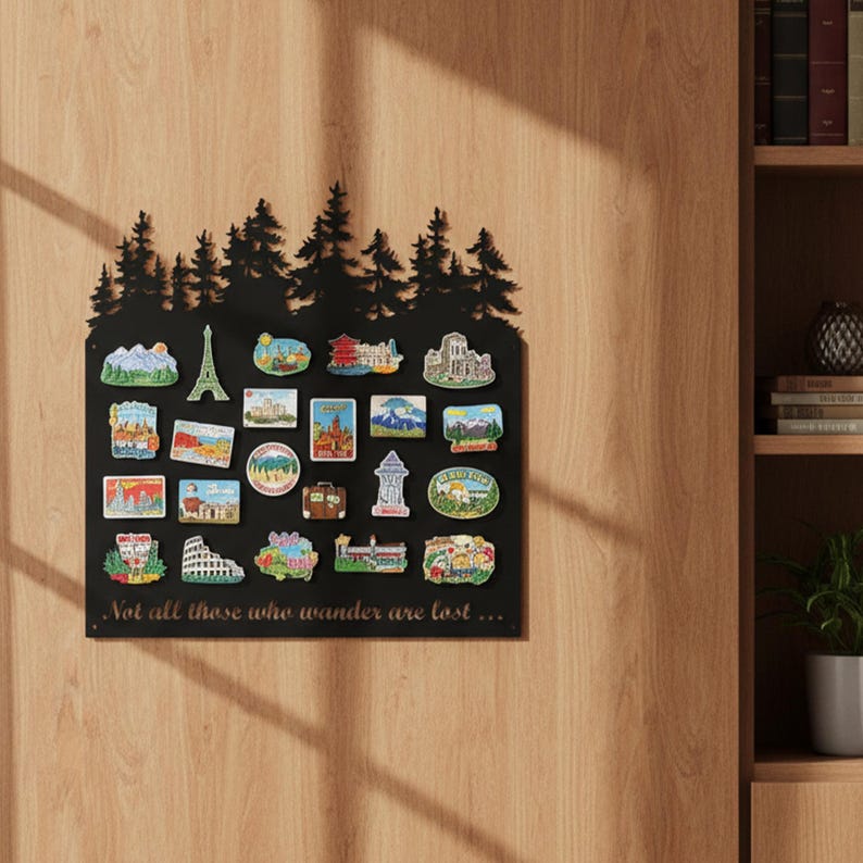 May include: A black metal magnet board with a silhouette of pine trees at the top. The board displays colorful travel-themed magnets, including landmarks like the Eiffel Tower. The quote "Not all those who wander are lost..." is printed at the bottom.