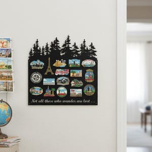 May include: Black metal souvenir display board with a forest silhouette at the top. The board holds various colorful souvenir magnets depicting landmarks and travel destinations. The quote "Not all those who wander are lost..." is printed at the bottom.