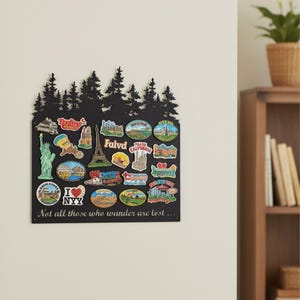 May include: A black metal wall decor piece with a forest silhouette at the top. It features various travel-themed magnets, including the Statue of Liberty, the Eiffel Tower, and the text "I NYY". The text "Not all those who wander are lost..." is at the bottom.