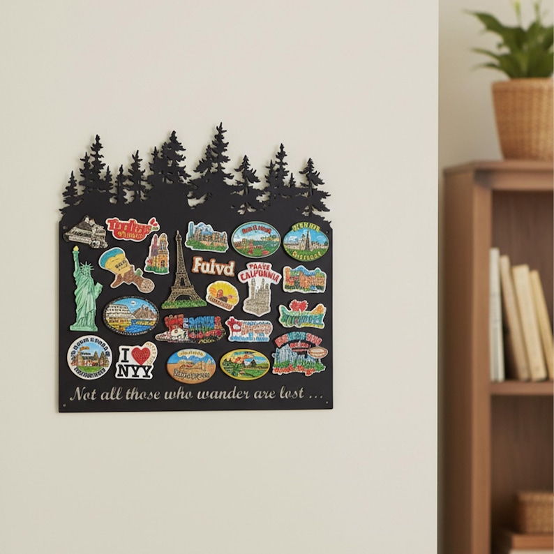 May include: A black metal wall decor piece with a forest silhouette at the top. It features various travel-themed magnets, including the Statue of Liberty, the Eiffel Tower, and the text "I NYY". The text "Not all those who wander are lost..." is at the bottom.