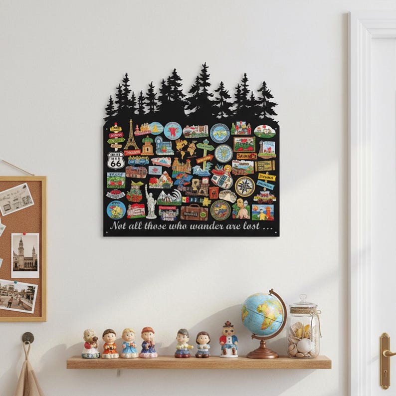 May include: Black metal wall art featuring a silhouette of pine trees at the top and numerous colorful travel-themed magnets. The phrase "Not all those who wander are lost..." is written in white script. A wooden shelf below displays figurines and a globe.