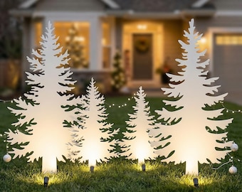 May include: Four white, flat, silhouette-style Christmas tree decorations arranged in a row on a lawn. Each tree features a jagged, pine-like outline and is illuminated from the base with warm white light, connected by a string of small lights.