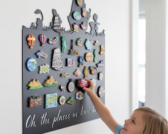 May include: A black magnetic board with a silhouette design and the phrase "Oh, the places we have been" in white script. The board displays travel-themed magnets, including landmarks and hot air balloons.