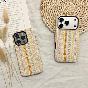 Puede incluir: Dos fundas de teléfono con un estampado floral. Las fundas presentan un diseño con rayas verticales en amarillo, rosa y blanco, con un estampado de cuadros en el centro. Las fundas están sobre una superficie blanca.