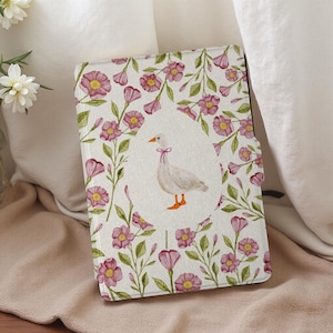 May include: A white goose with a pink ribbon around its neck stands on a white background with pink flowers. The goose is surrounded by a floral pattern of pink flowers and green leaves.