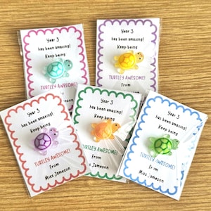 May include: Five small cards with scalloped edges, each holding a colourful turtle pin. The cards display the text "Year 3 has been amazing! Keep being" and "TURTLEY AWESOME!" with a name. The turtle pins are in blue, yellow, orange, purple, and green.