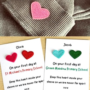 May include: A pink heart-shaped patch is attached to a grey striped fabric. Two cards are displayed, one with the name "Olivia" and two red heart patches, and the other with "Jacob" and two heart patches, one teal and one green. Text on the cards reads "On your first day at" and "Keep this heart inside your sleeve so we are never far apart."