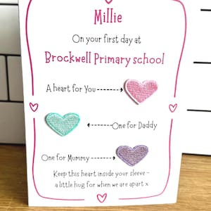May include: A white greeting card with pink borders and text reading Millie On your first day at Brockwell Primary school. It features three embroidered heart patches in pink, teal, and purple, with arrows pointing to text labels A heart for You, One for Daddy, and One for Mummy, plus the text Keep this heart inside your sleeve - a little hug for when we are apart x.