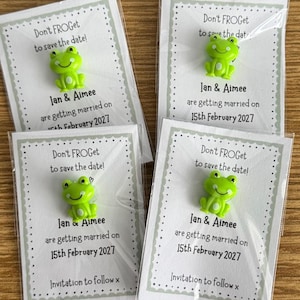 May include: Four wedding save-the-date cards, each with a green frog embellishment. The cards read "Don't FROGet to save the date!" and announce a wedding on February 15th, 2027, for Ian & Aimee. The cards are in clear plastic.