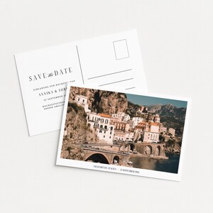 May include: Two white postcards. One features a scenic photo of a coastal town with a bridge. The other postcard has the text "SAVE the DATE" and wedding details. The photo shows a town on a cliffside.